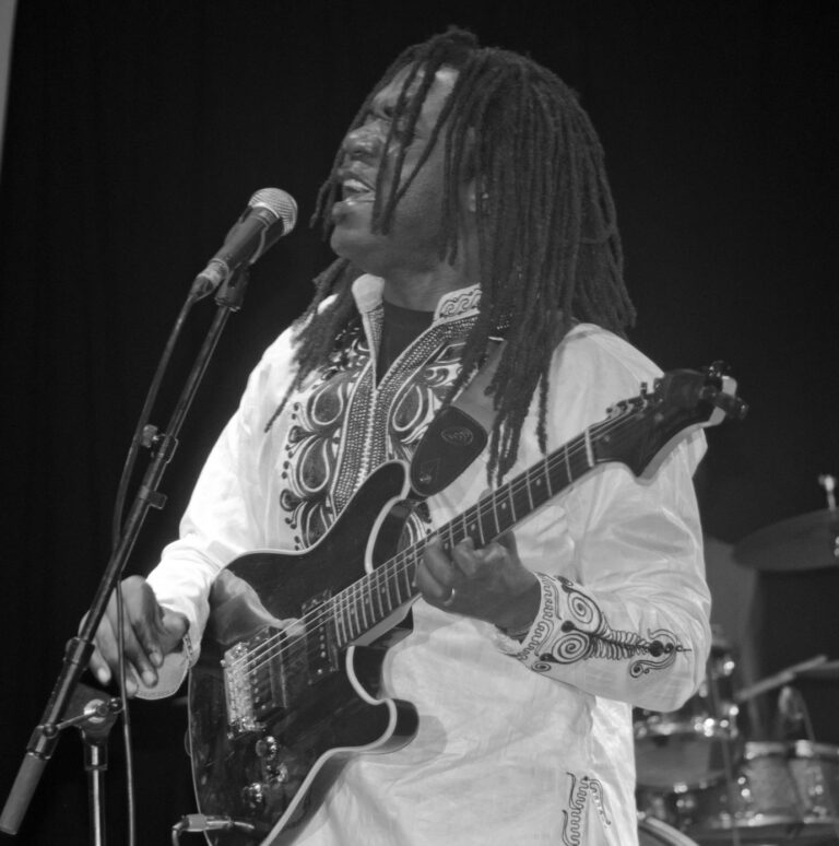 Armand Ntep singing and playing guitar on stage